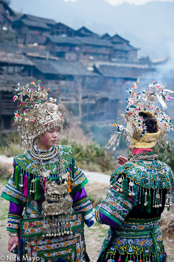 Two Dong girls wearing traditional wedding clothes, including aprons, headdresses and necklaces, in the village of Shao Dong.