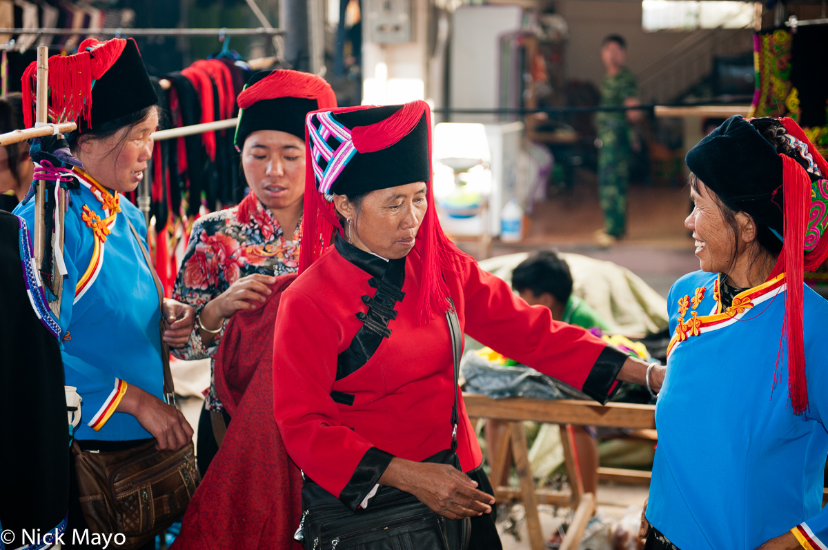 Hani women trying on clothes and hats at a stall in Da Hei Shan market.