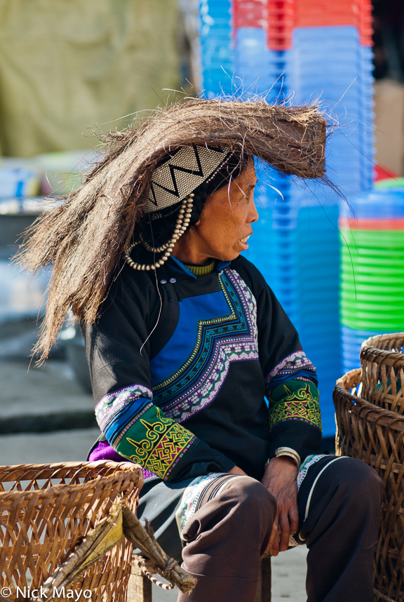 A Hani woman, using natural fibre as a hat, sitting between her baskets at Pinghe market.