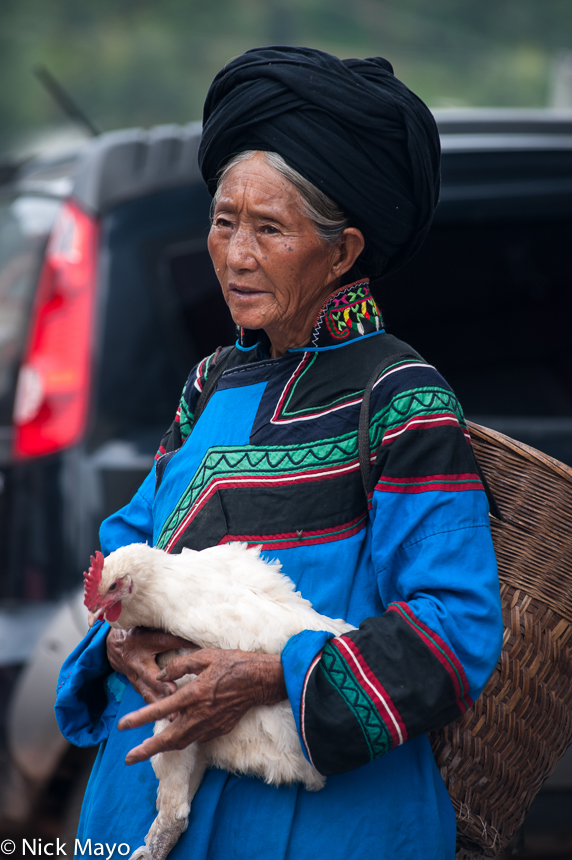 An older Yi lady holding a chicken at Tuo Mu market in Daliangshan.