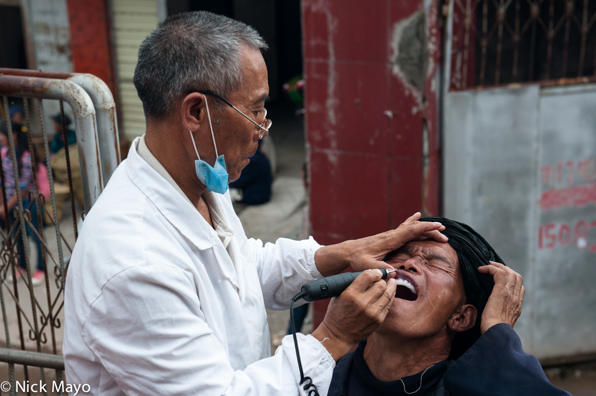 A Han dentist at work on a Yi patient at the Yi market of Tuo Mu Guo in Daliangshan.