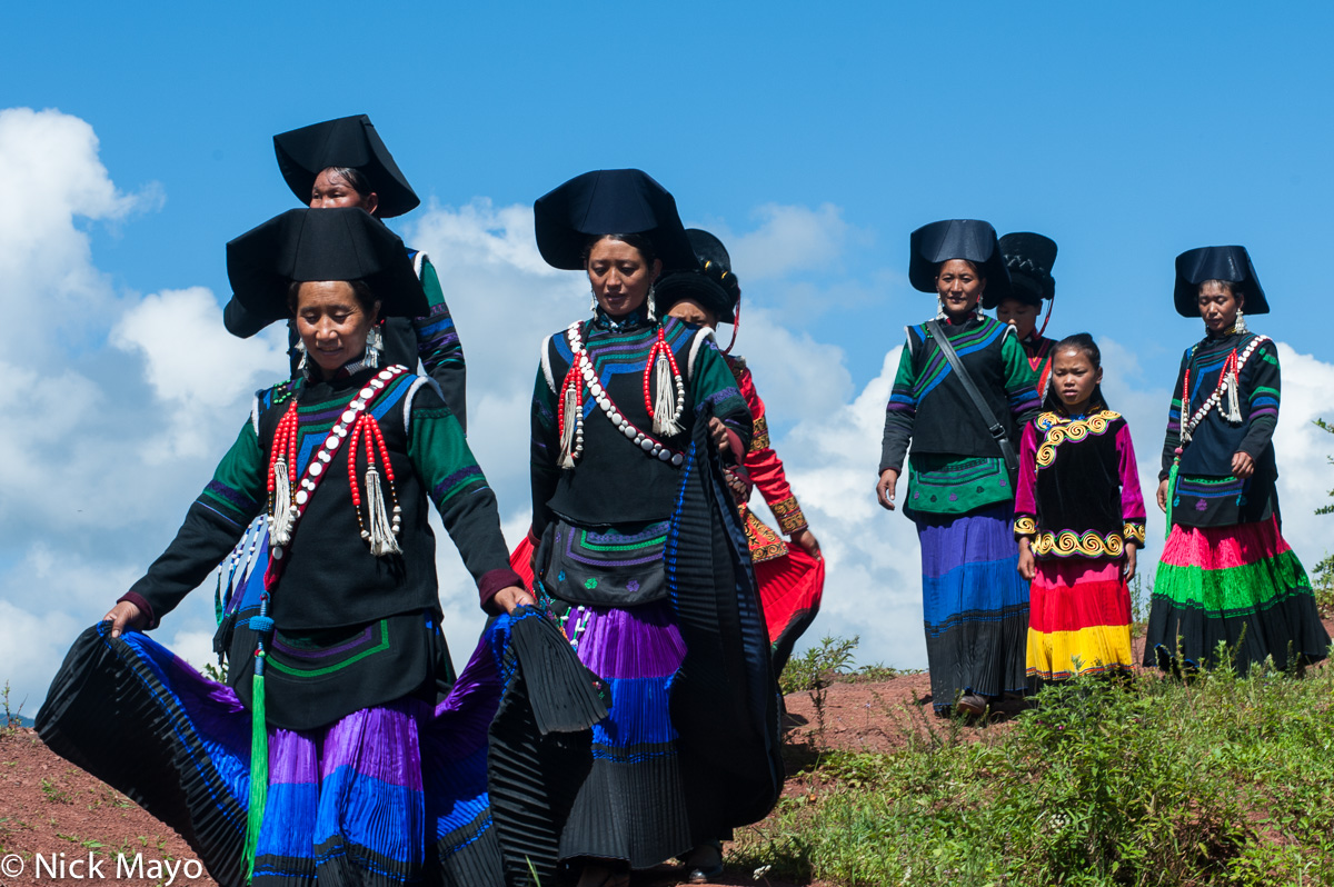 A group of Yi funeral greeters, wearing traditional clothes, hats, necklaces and earrings, at Mi Shi Qing Mo in Daliangshan.