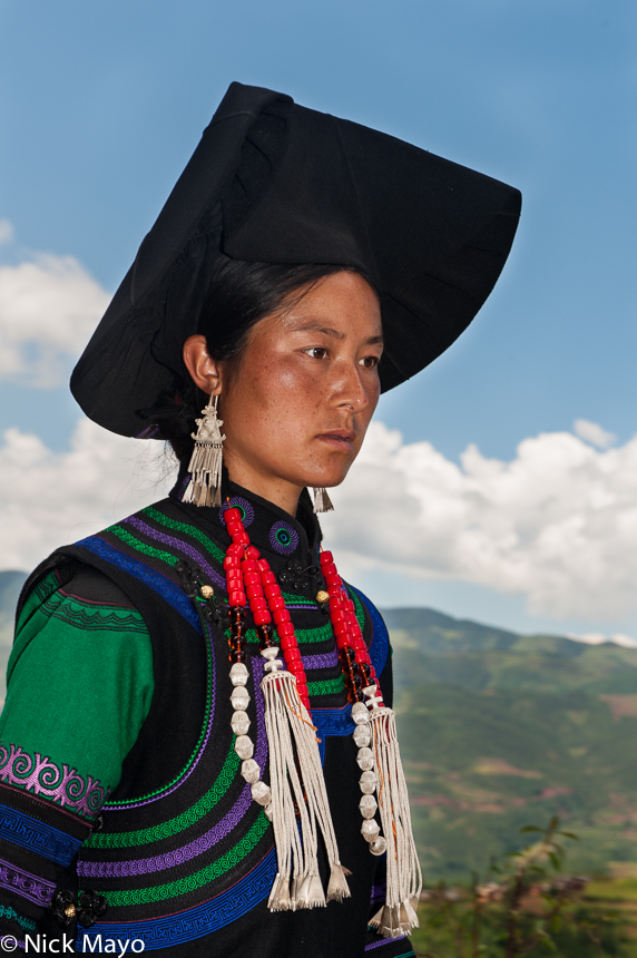 A female greeter, wearing traditional clothes, hats, necklaces and earrings, heading to a Yi funeral at Mi Shi Qing Mo in Daliangshan...