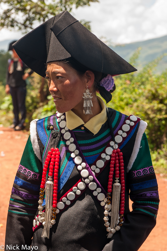 A female greeter, wearing traditional clothes, hats, necklaces and earrings, at a Yi funeral at Mi Shi Qing Mo in Daliangshan...