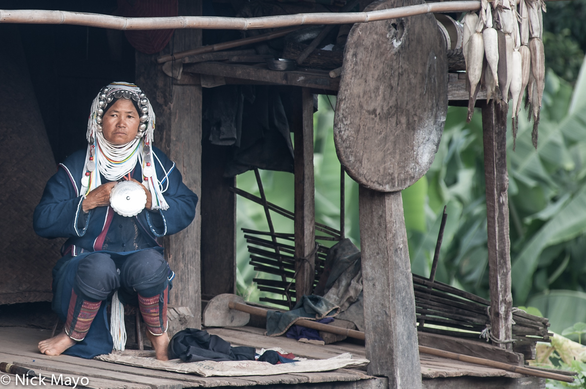 An Akha (Hani) woman wearing a traditional headdress on the terrace of her house in the village of Hoi Yang II.