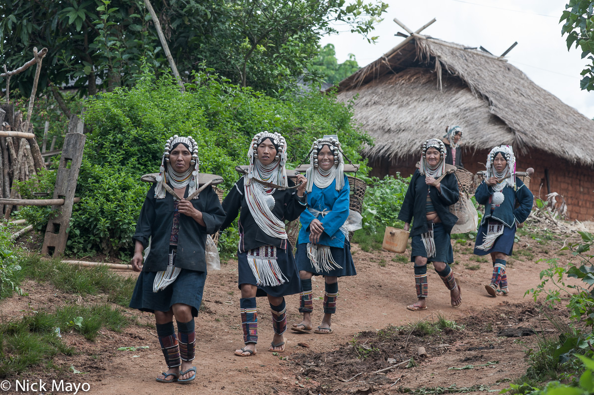 Akha (Hani) women walking past a thatched house on their way to the spring in the village of Hoi Yang II.