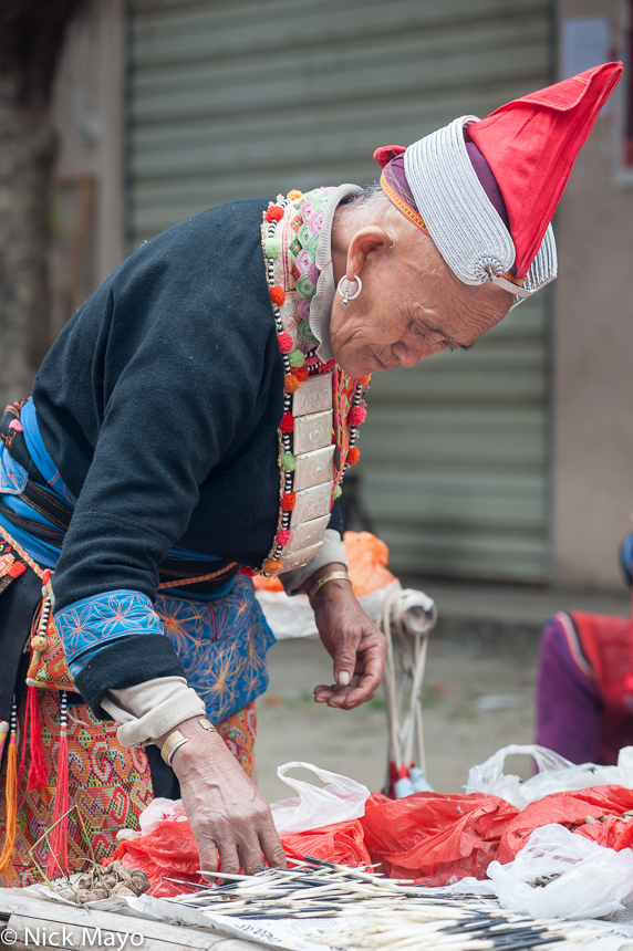 A Hongte Yao vendor, wearing a traditional hat, breastpiece, earring and bracelet, at Mengla market.