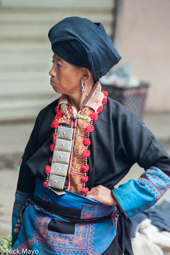 A Butuo Yao woman, wearing a traditional turban, earring and breastpiece, at Mengla market.