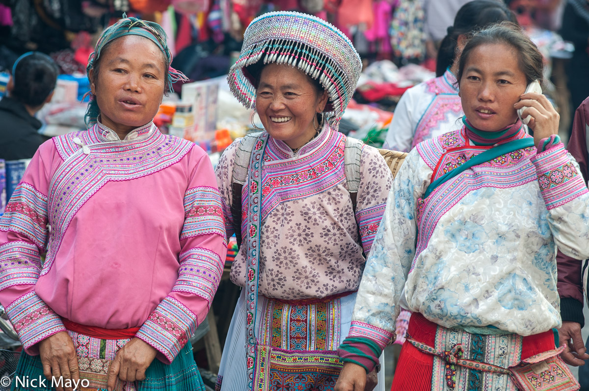 Three Miao women, one wearing a traditional hat and oversized earrings, in Baihe.