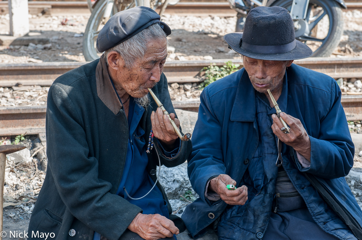 Two men smoking brass pipes by the tracks in Baihe.