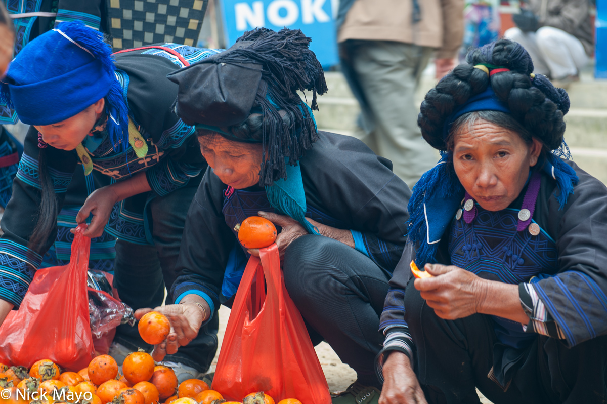 Hani women wearing decorative hair pieces shopping for oranges in Maandi market.