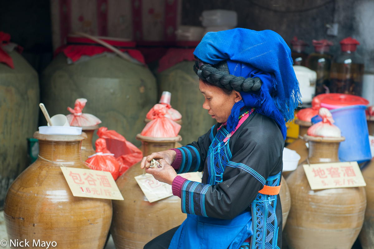 A Hani woman shopping for home brewed liquor stored in wine jars at Maandi market.