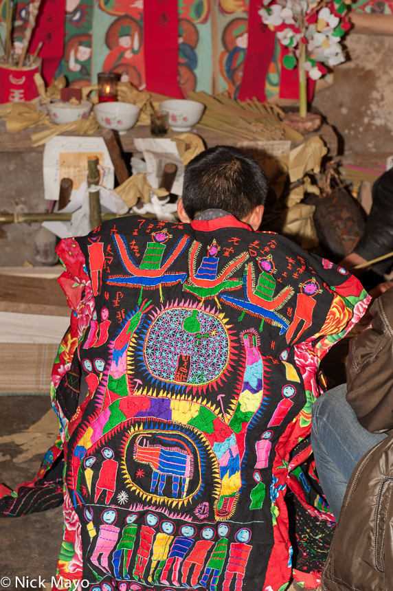 A Yao priest (sai mienh) in a traditional robe kneeling before the altar at a dujie in the village of Ku Ju Jie.