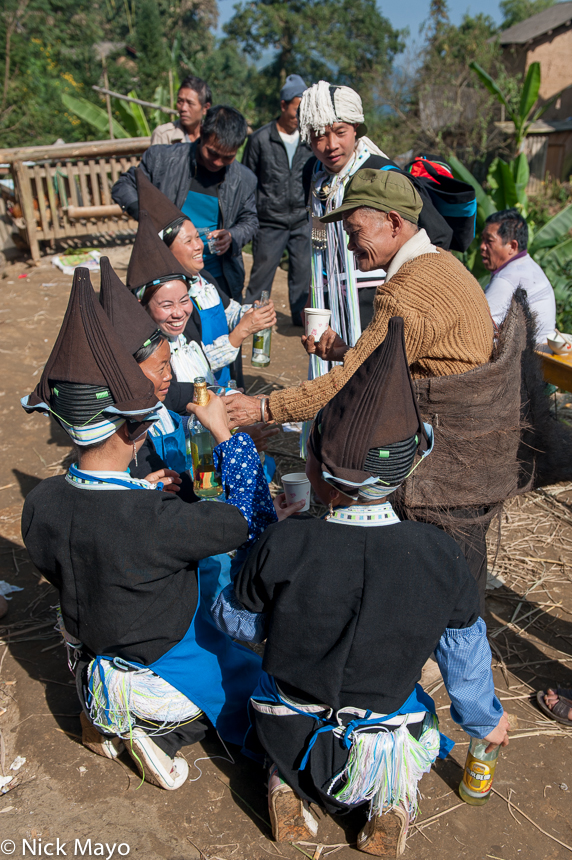 Yao woman in traditional hats ceremonially pouring beer to a man after a dujie in the village of Ku Ju Jie.