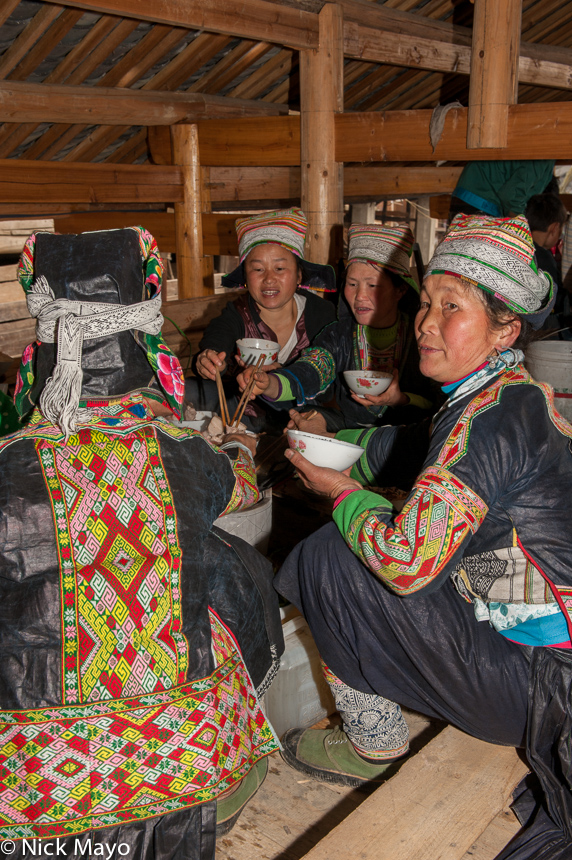 Miao women, in traditional dress, hats and earrings, eating a wedding lunch in the village of Yangweng.