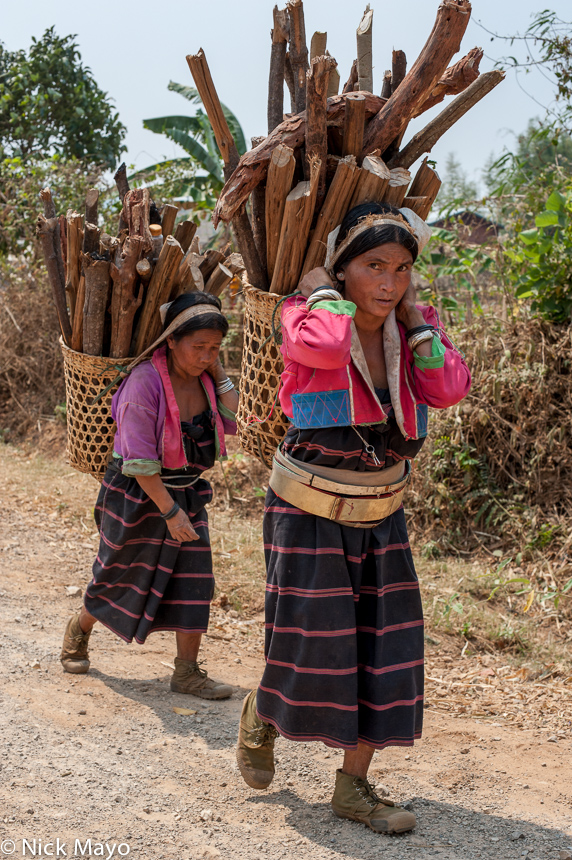 Palaung women wearing traditional waist hoops carrying firewood home to the village of Namgyen in backstrap baskets.