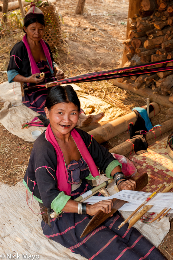 Two women wearing traditional bracelets weaving on back looms in the Palaung village of Ban Nong.