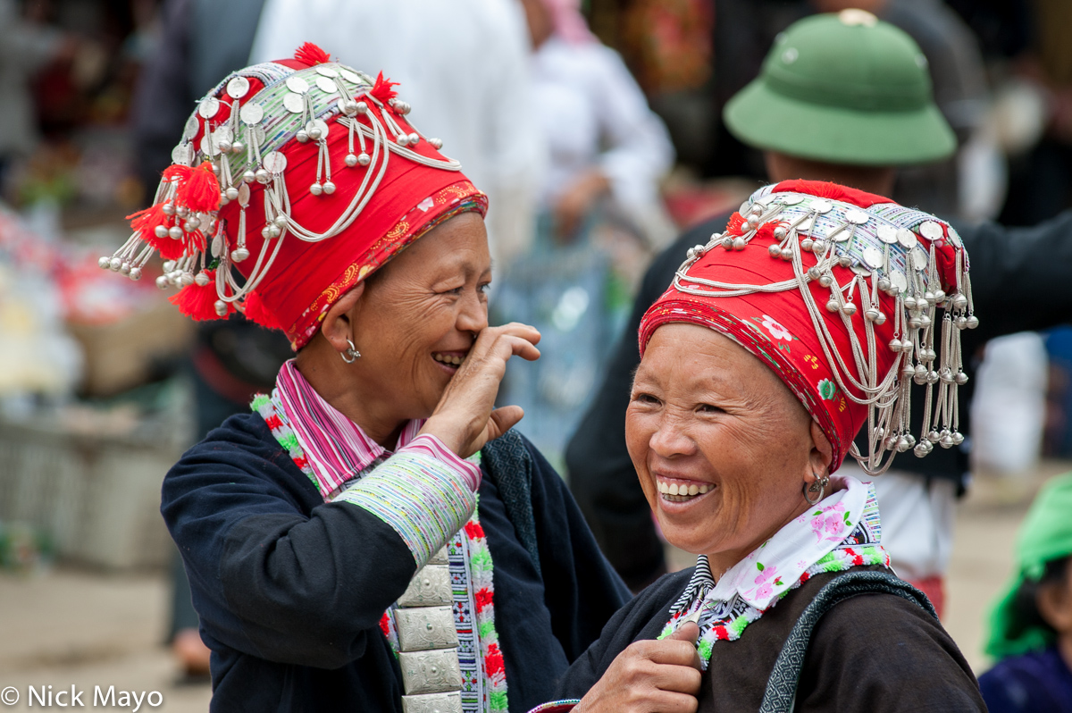 Two Red Dao (Yao) women, in their traditional dress, earrings and hats, at Muong Hum on market day.