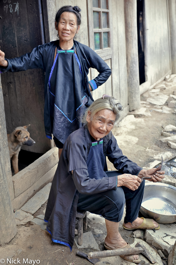 A dog and two women with their hair done up in top knots in the Dong village of Wuei.