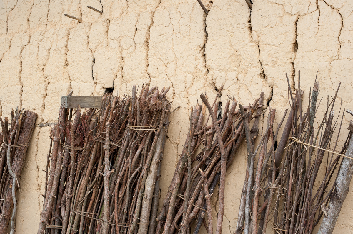 Firewood leaning against the cracked wall of a mud brick house at Lao Va Chai.