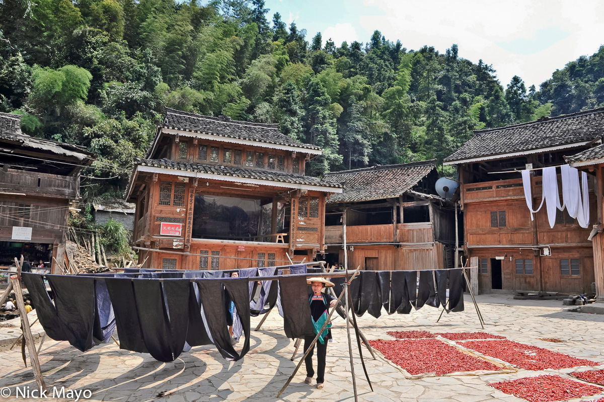 Freshly indigo dyed cloth drying alongside clilis laid out in front of the opera stage at the Dong village of Yintan.