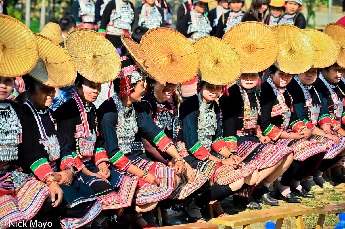 A line of Hua Yao Dai woman wearing traditional breastpieces and hats waiting to dance at a festival in Mosha.