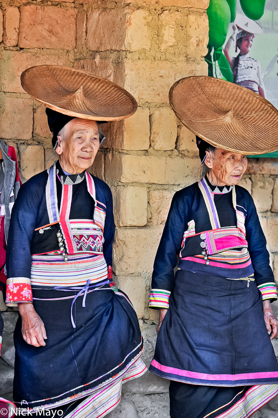 Two Hua Yao Dai women wearing traditional clothes, hats and breast plates observing a festival in Mosha.