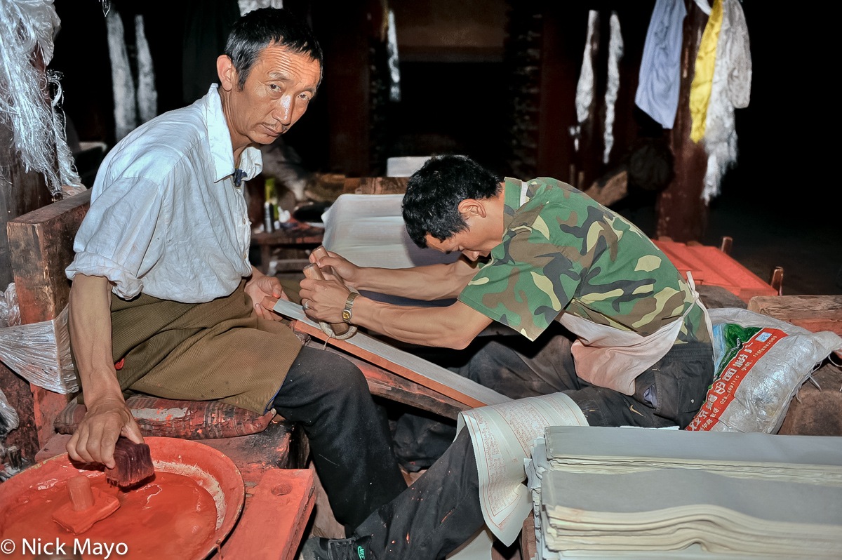 Two men hand printing scriptures from wooden blocks at the Derge Printing House.