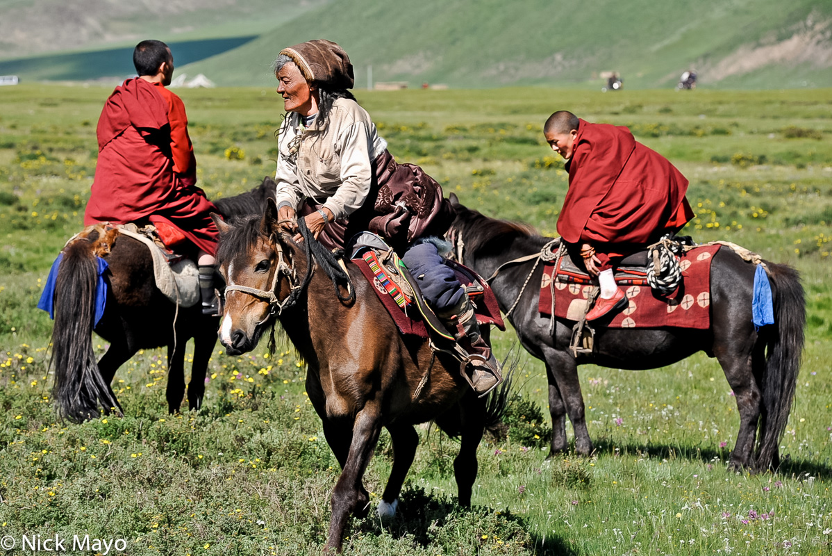 Two young Tibetan monks and an older lady on horseback at a horse festival in Sershul.