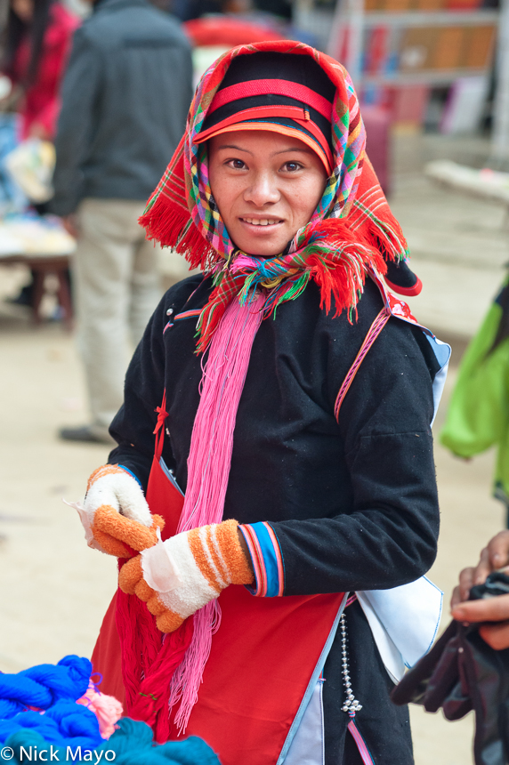 A Yao woman, traditionally attired with a hat and red and blue bag, shopping at Nafa market.