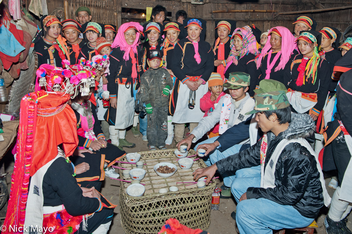 Female guests watching the groom's family offering a symbolic drink and bowl of meat to the bride's mother at a wedding celebration...