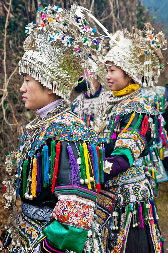 Two Dong girls, wearing crown headdresses, breastpieces and silver necklaces, awaiting the bridal procession at a wedding in...