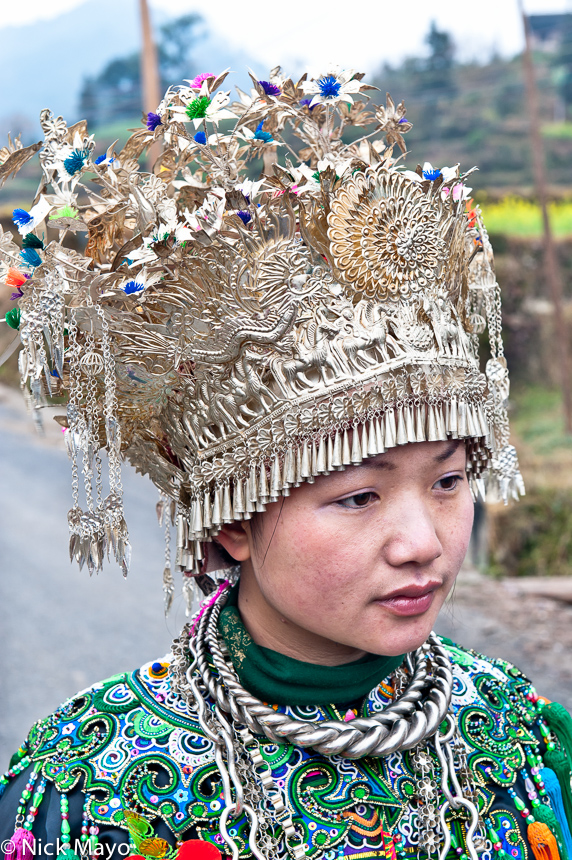 A Dong bride to be wearing a crown headdress and silver necklace on her way to her wedding in Yudong.