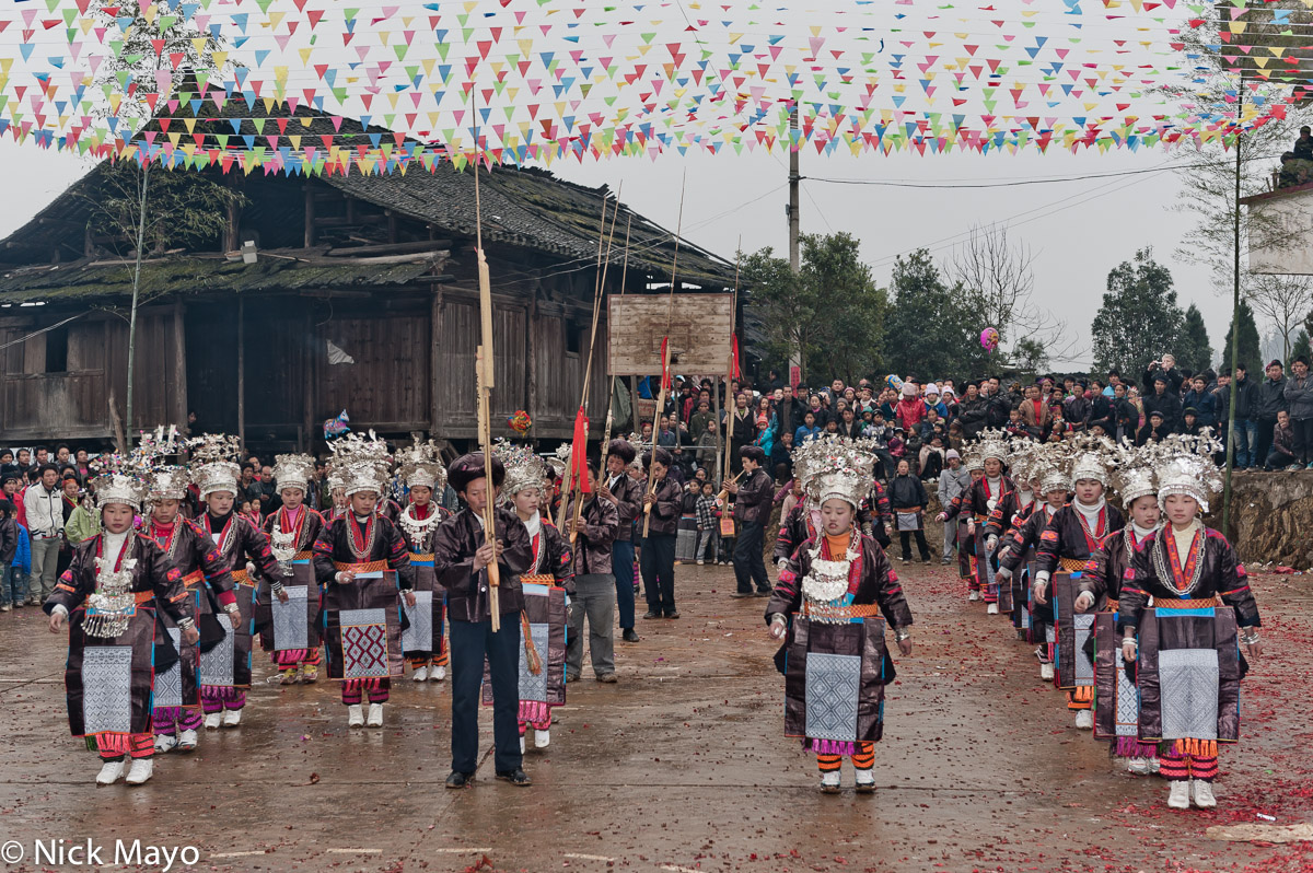 Unmarried Miao girls, wearing festival attire of crown headdresses, breastpieces, necklaces and embroidered aprons, dancing to...