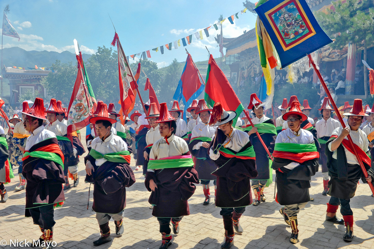 Tibetan men, wearing red tasselled hats and carrying standards, participating in a monastery festival in Rongpo Gyakhar.