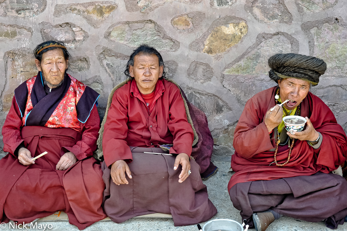 Three Tibetan monks, one eating lunch, at a grassland monastery in Jadir.