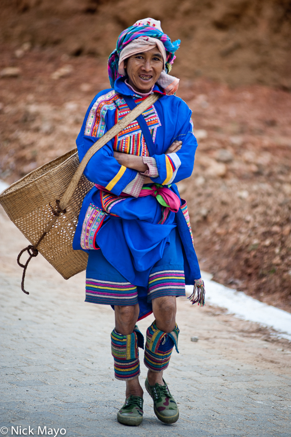 A Lahu woman from Nanmei, in traditional clothes and leggings, walking to market with her backstrap basket.