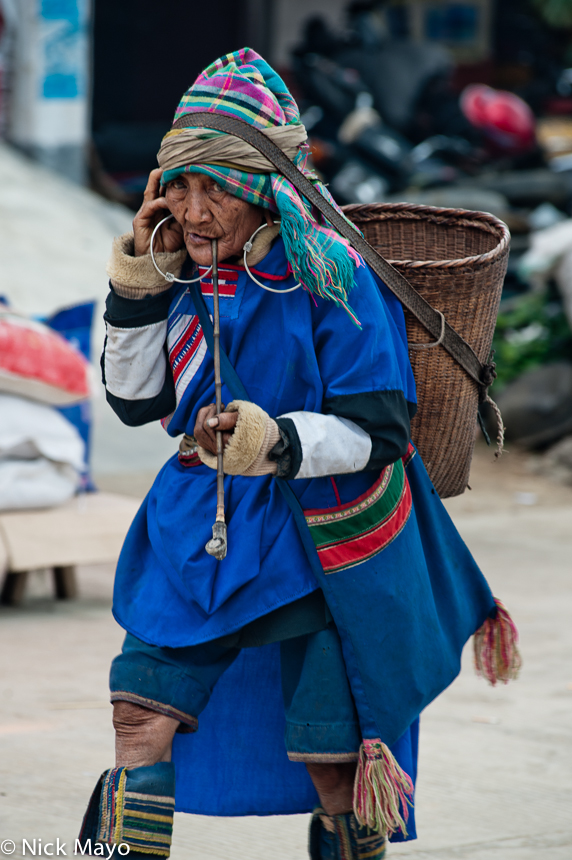 A Lahu woman with a backstrap basket smoking a pipe while shopping at Nanmei market. 