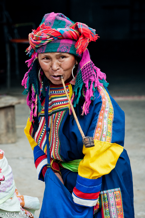 A Lahu woman, in traditional dress and earrings, smoking a pipe at Nanmei market.