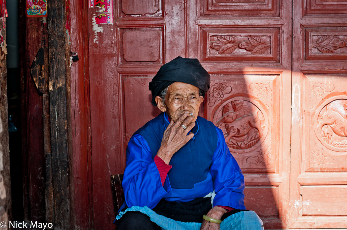 A Lama Bai woman from Ing Pan, in traditional dress and turban, smoking a cigarette.