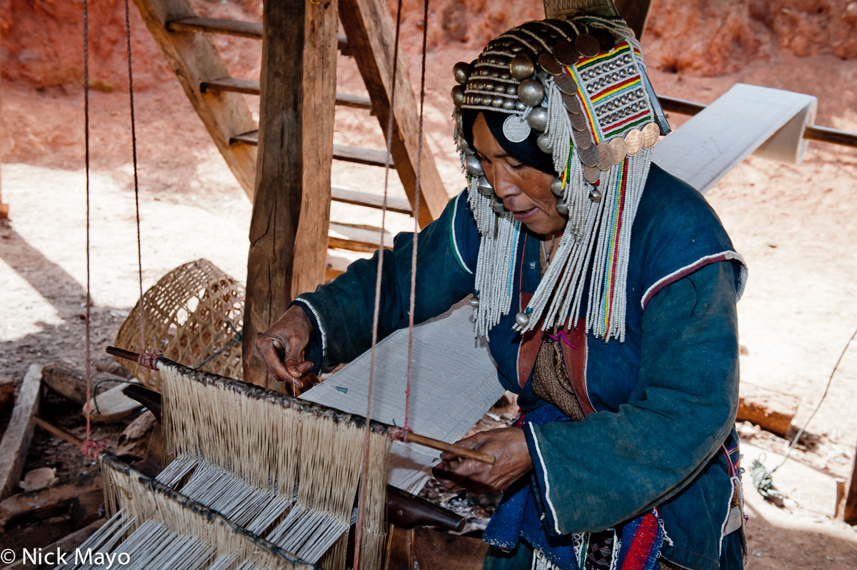 An Akha (Hani) woman, wearing a traditional headdress, weaving cloth on a foot treadle loom in the village of Hoi Yang II.