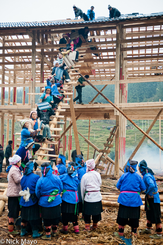 Traditionally dressed Miao women assisting in the construction of the roof of a house located near Bakai.