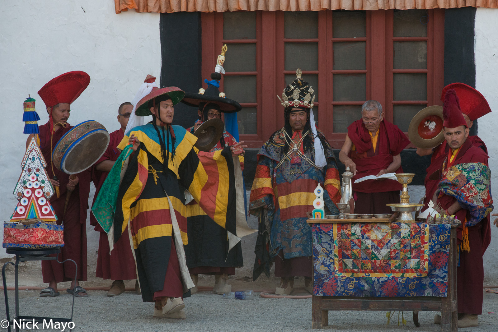 Monks with cymbals, a drum and a scripture performing a ritual next to a butter sculpture at the annual Phyang Tserup.