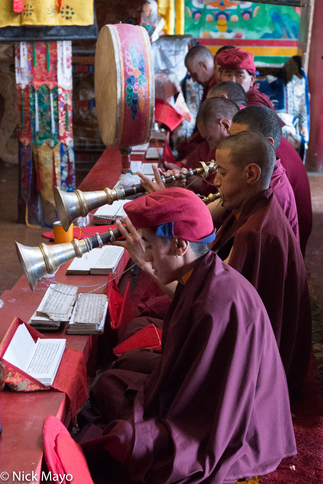 A Changpa monk in Korzok monastery chanting from a scripture while others play horns and a drum.