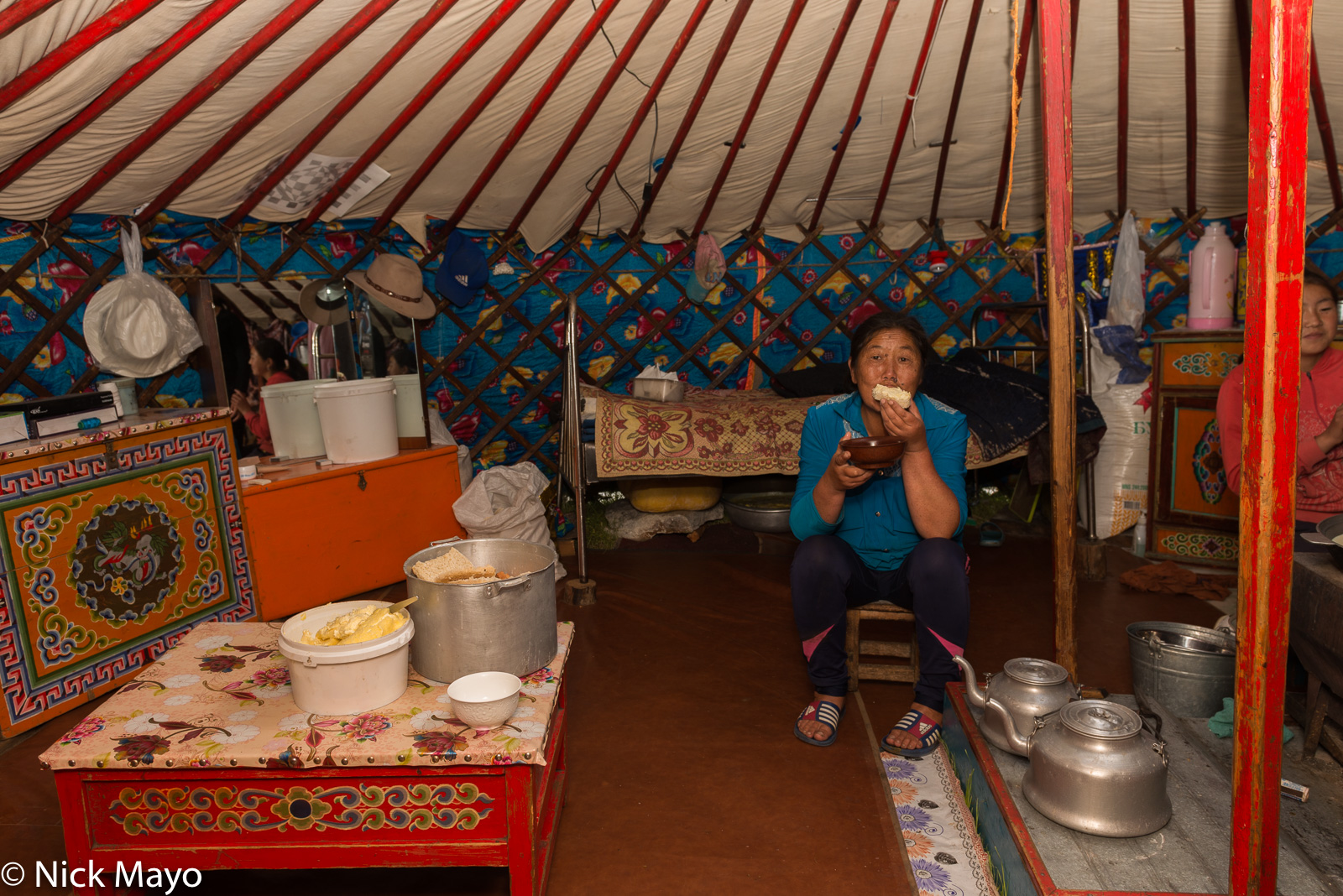 A Darkhad woman in her yurt on the Alag-Erdene steppe eating a breakfast of bread while kettles boil for tea.