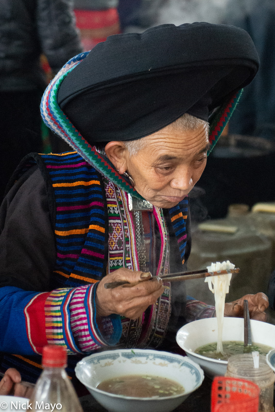 A Dao Ta Pan woman eating noodles at Lung Phin market.