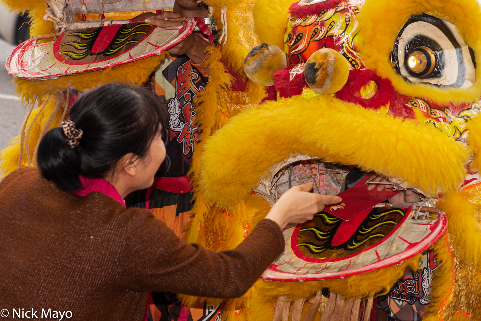 An offering of a red envelope with money inside being handed to a lion dancer through the mouth of his costume in an event organized...