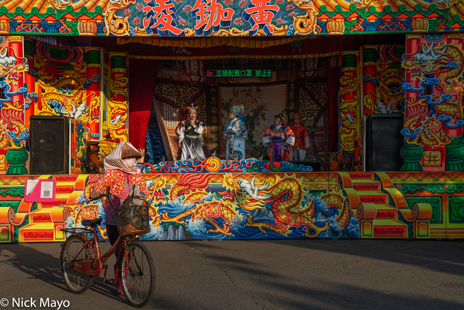A woman pushing her bicycle past a ke-tse opera performance at the Wulong temple in Tailiao in Changhua County.