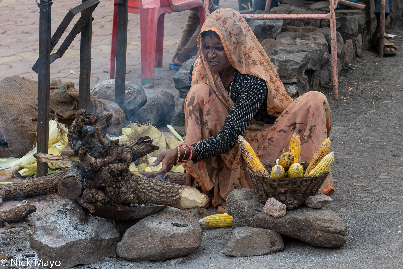 A Mandu street vendor preparing her fire to roast corn cobs.