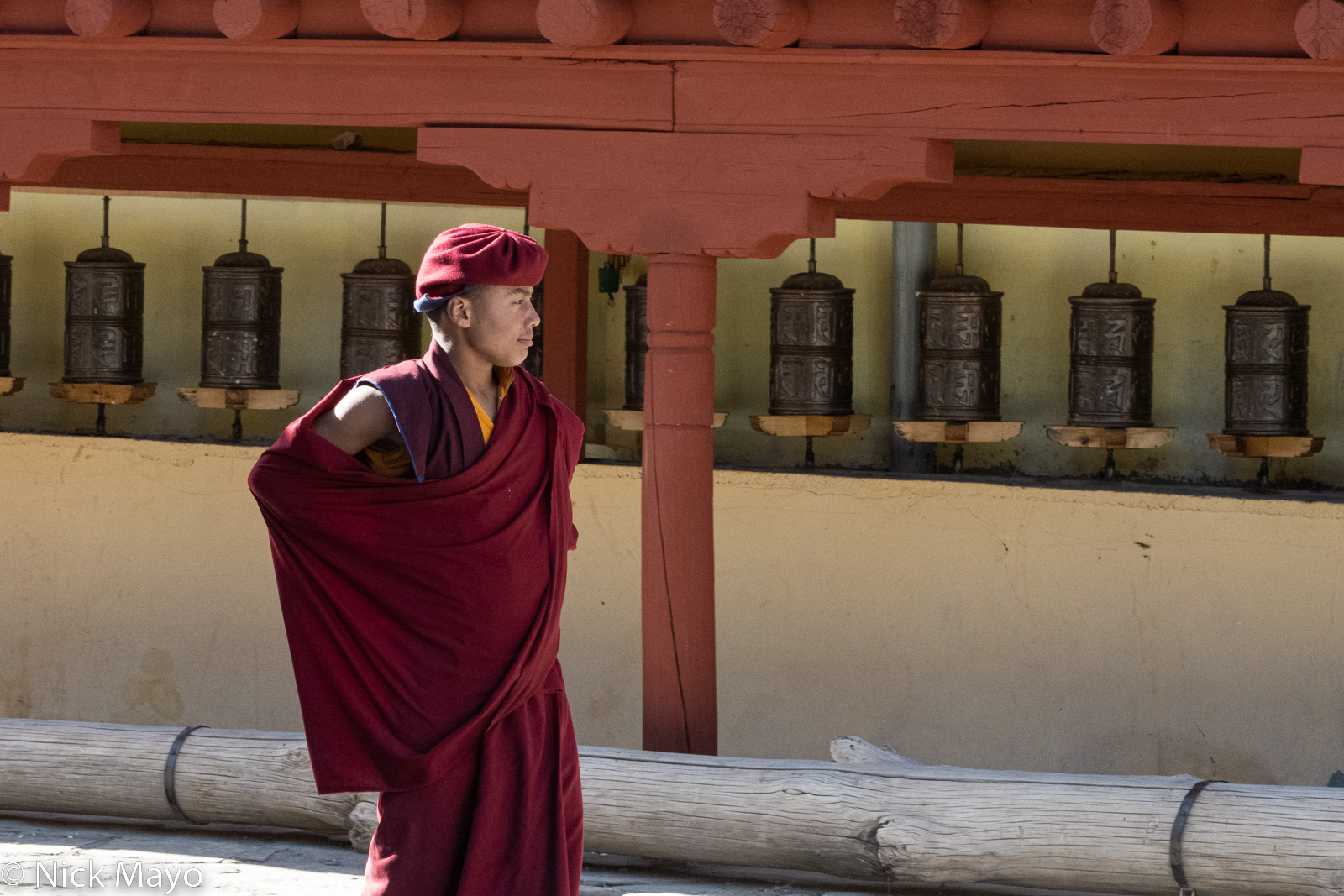 A Hemis monastery monk standing beside the wall of prayer wheels.